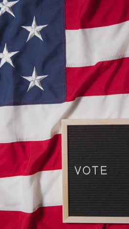 Vertical-Video-Of-Sign-Reading-Vote-Lying-On-US-Stars-And-Stripes-Flag-For-American-Election-2024-2